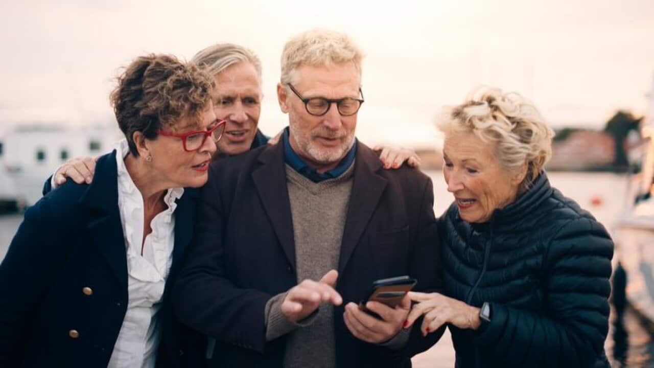 Senior male and female friends using smart phone while standing at harbor
