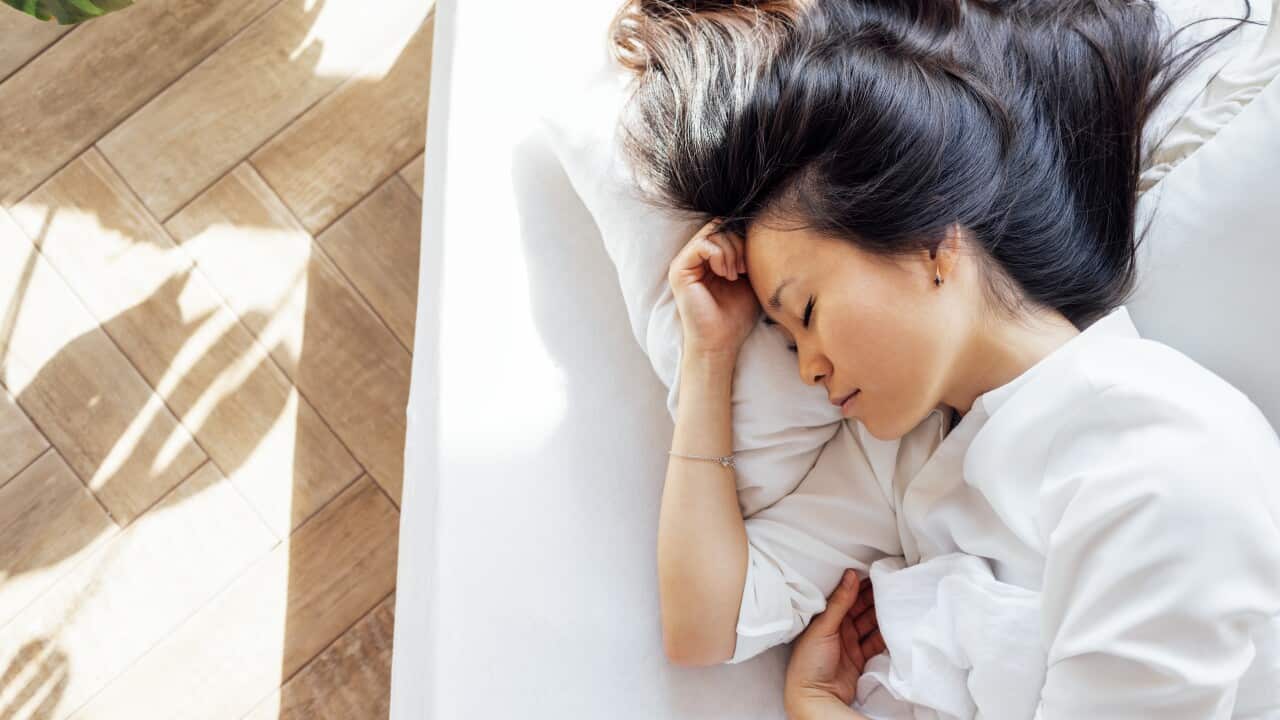 Attractive happy Asian woman lies on a white linen bed in the mo