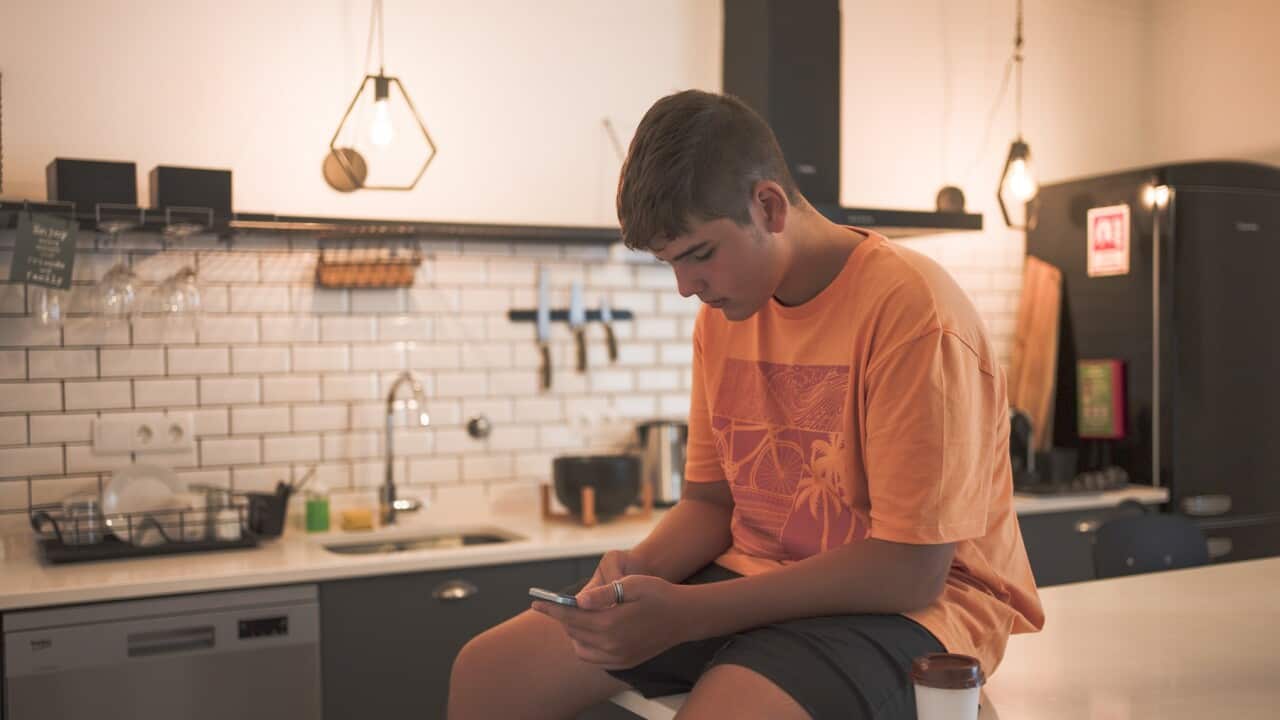 Teenage boy sitting at the kitchen table interacting with his smart phone while having a takeaway coffee