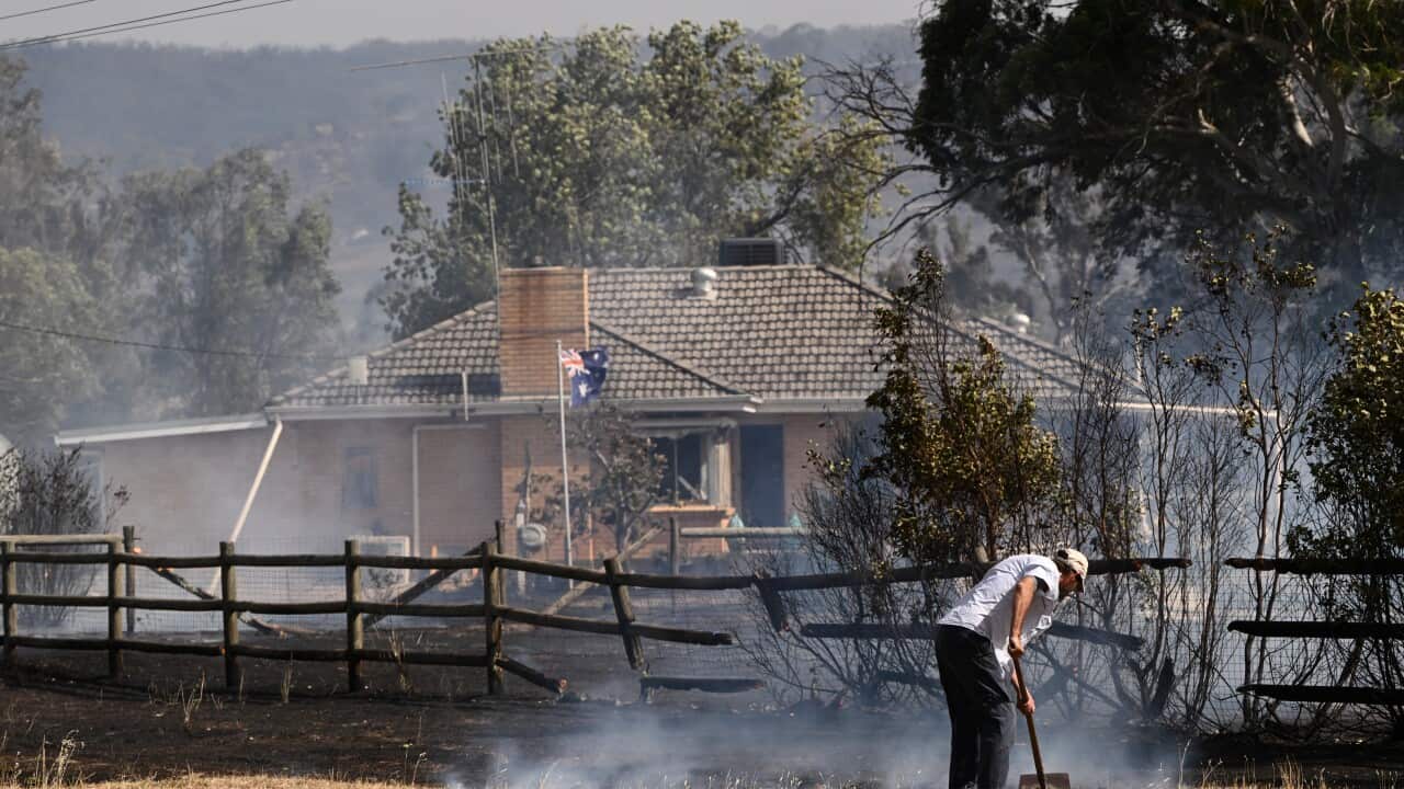 A man cleans land with a rake in front of a property surrounded by burnt out land.