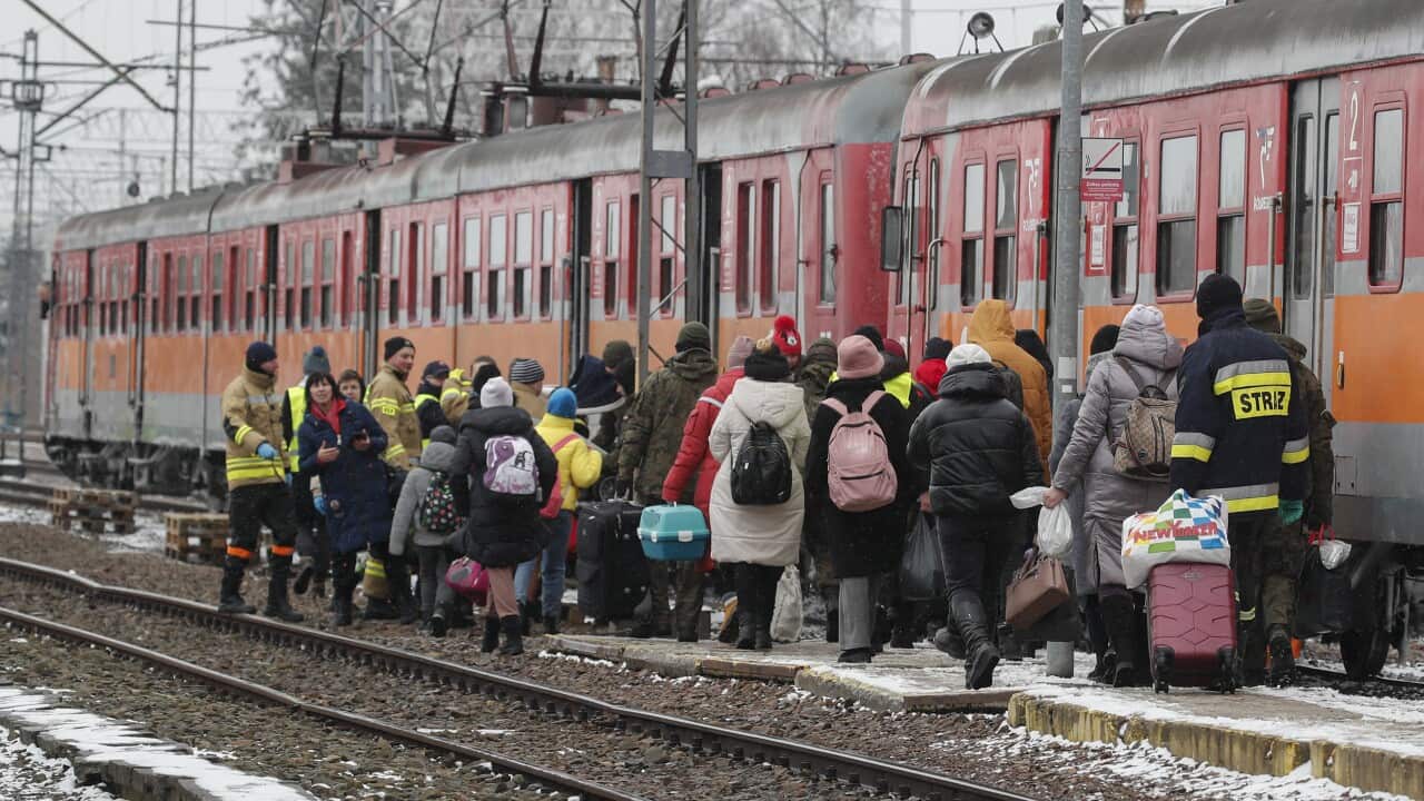 A crowd of people is seen at the side of a train.
