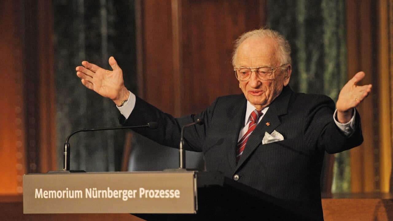 Benjamin Ferencz stands with hands outstretched as he delivers a speech at the lectern.
