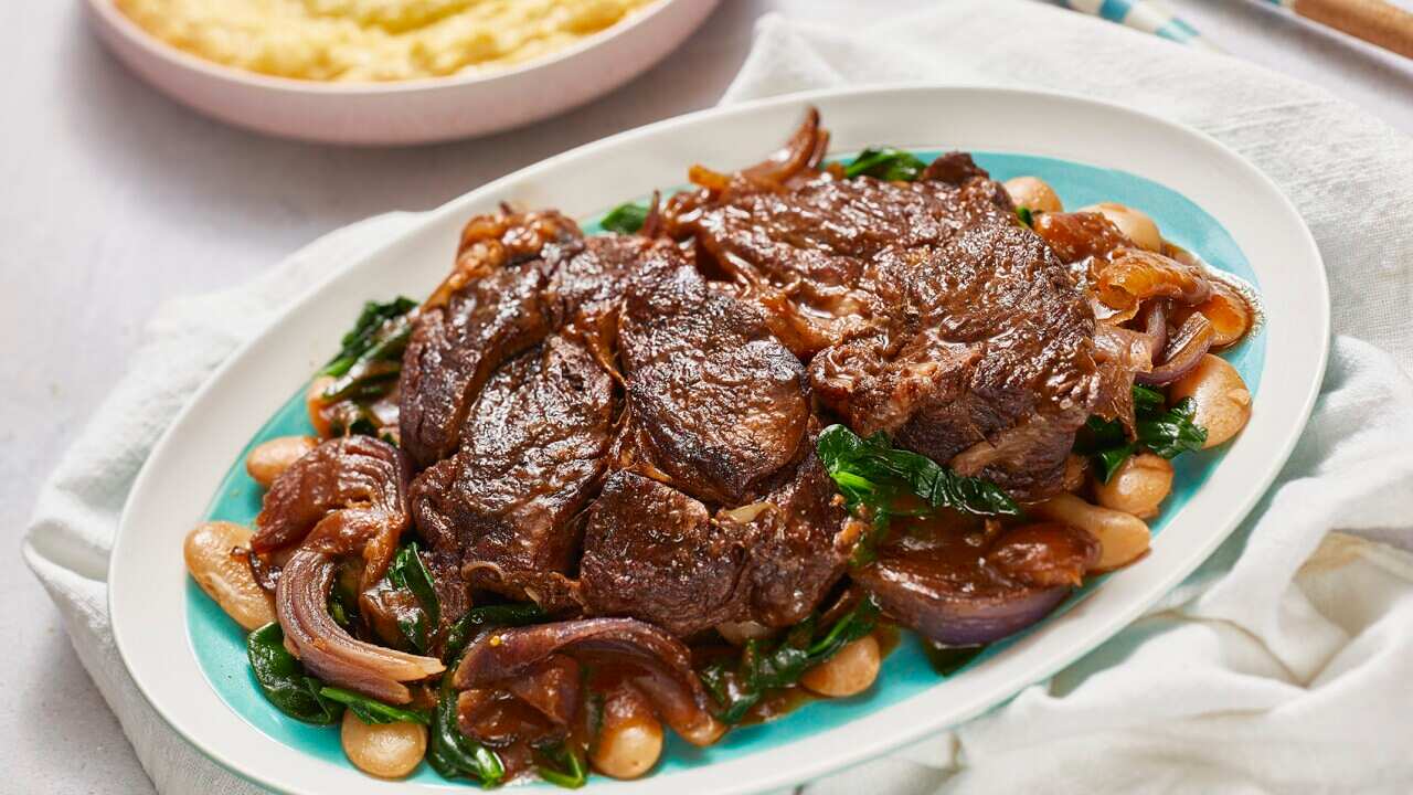 Chunky brown steaks, which look tender and moist, sit on a bed of butter beans and greens, on an oval platter.