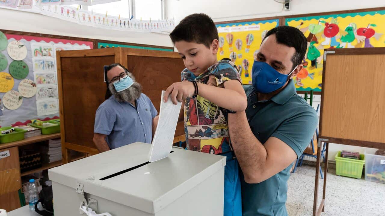 A Cypriot man holds his son up to cast his ballot at a polling station in Nicosia on 30 May, 2021.