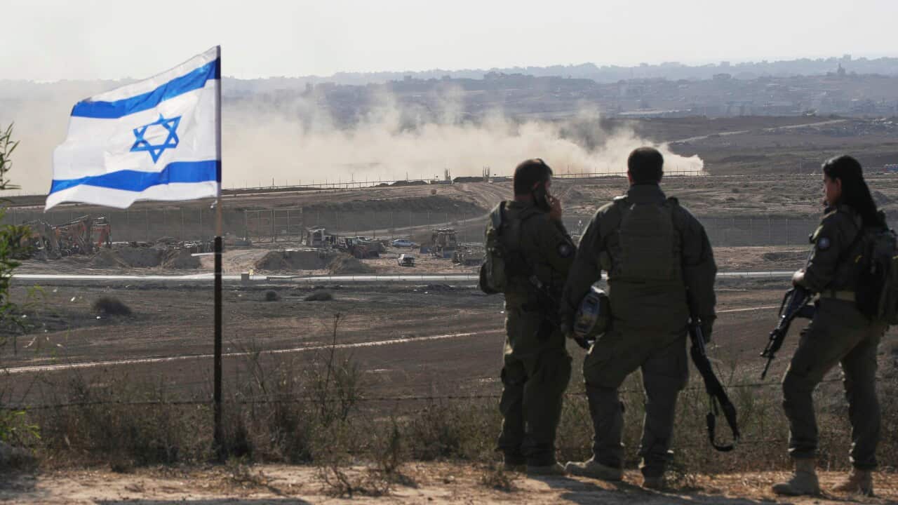 Soldiers standing in a rugged region next to an Israeli flag.
