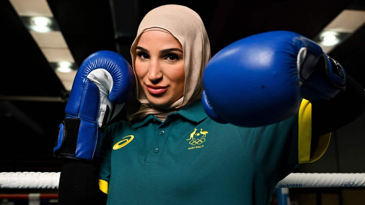 A woman in a hijab wearing a green polo shirt raising boxing-gloved fists
