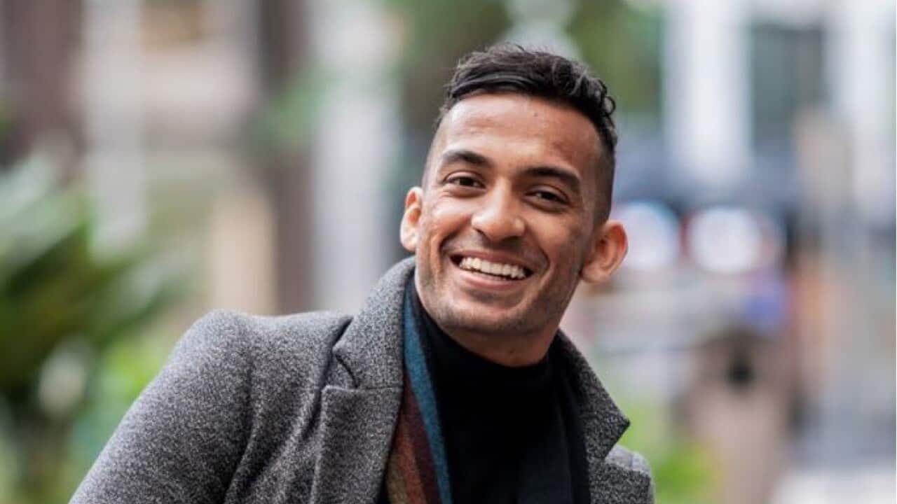 A man smiling wearing a grey coat and multi-coloured scarf 