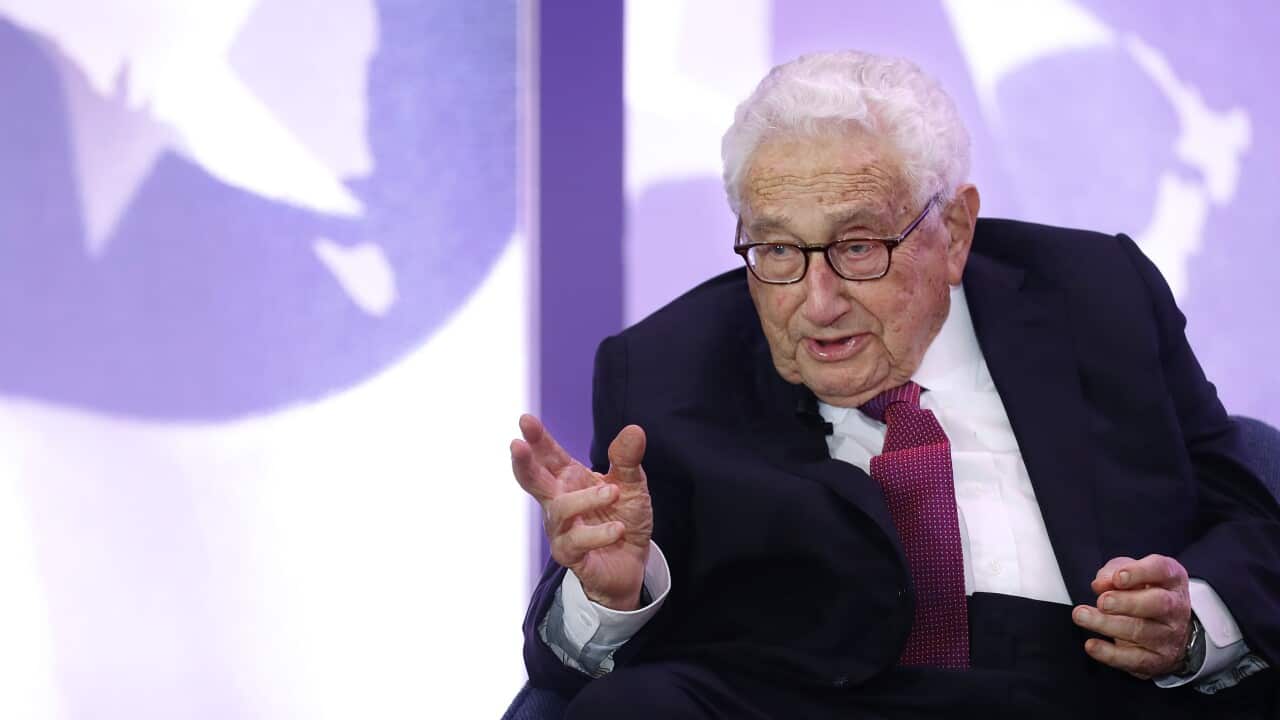 A man in a suit and maroon tie wearing glasses.