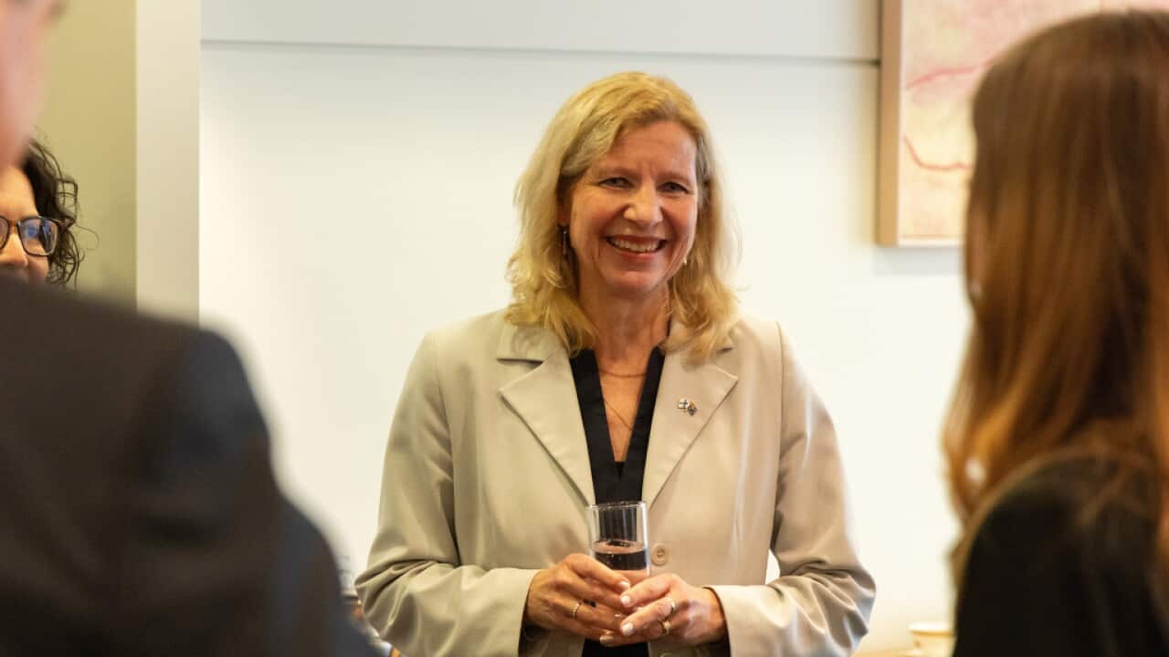A woman with blonde hair holding a glass of water looks forward smiling