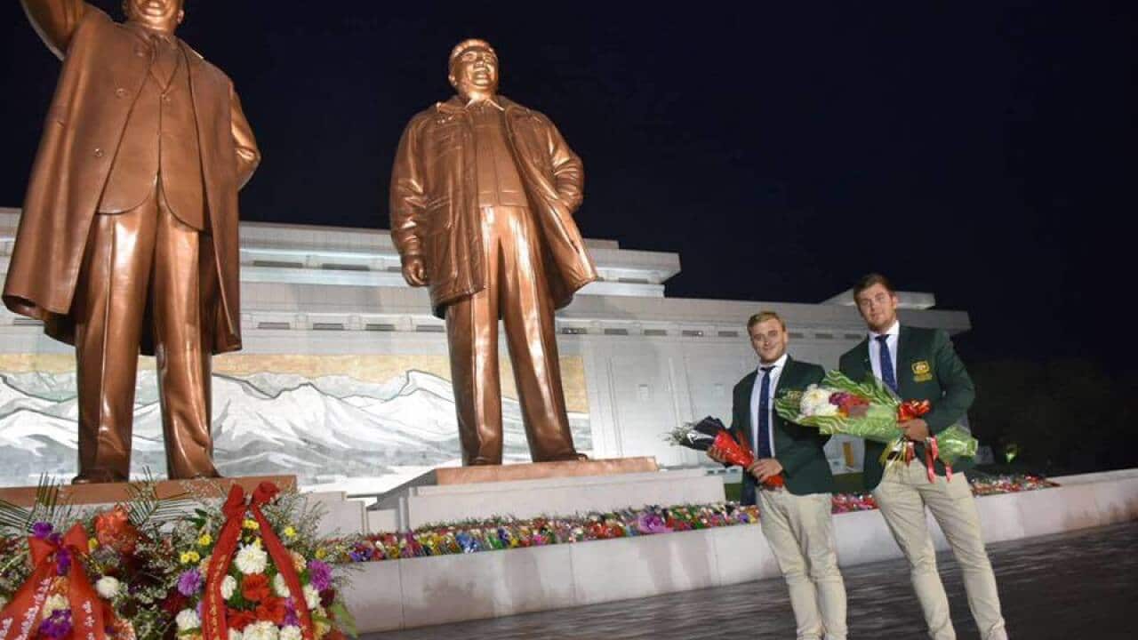 Morgan Ruig and Evan Shay place bouquets at a monument to the country's leaders in North Korea.