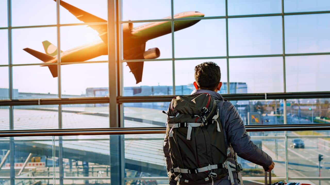 Male tourist is standing in airport and looking at aircraft flight through window.
