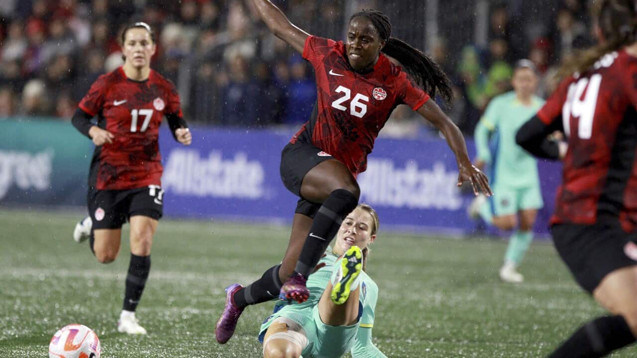 Three women in red football uniforms and one in a green uniform on a green ground