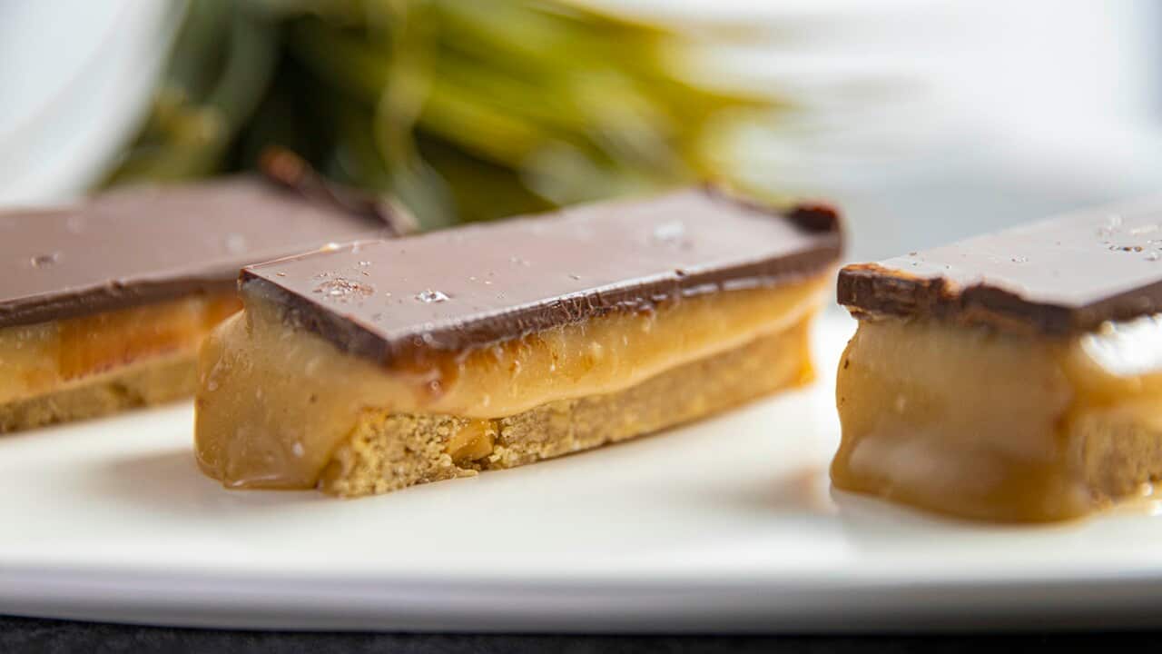 Rectangular fingers of a three-layer slice, with a gooey caramel centre, sit on a white plate.