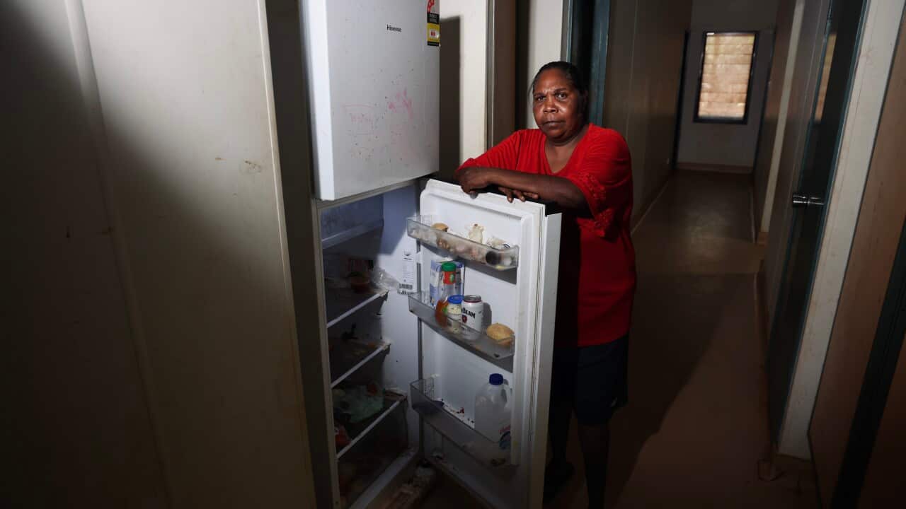 A middle-aged woman in a red top stands over her open fridge.