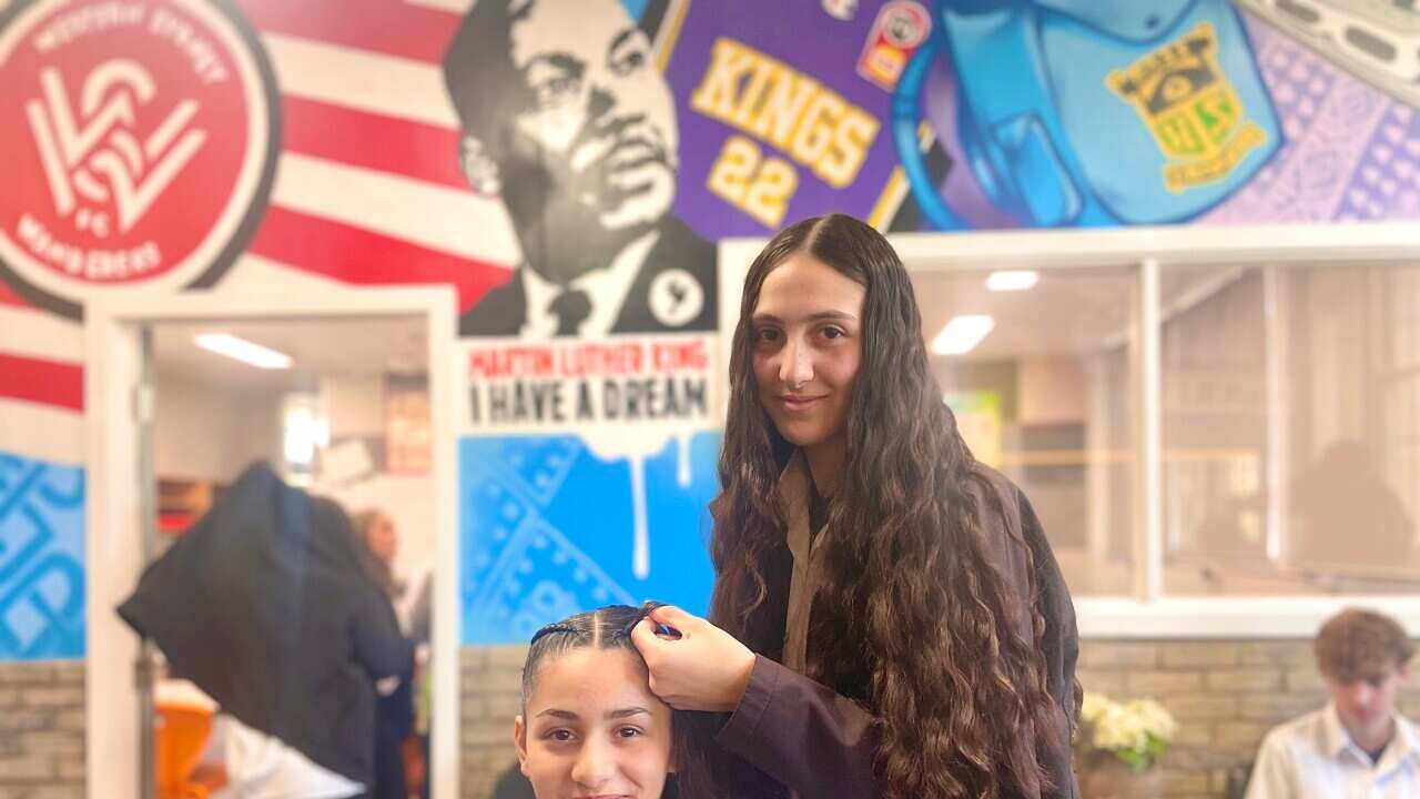 A girl braids her friend's hair in a hair salon with colourful murals. 