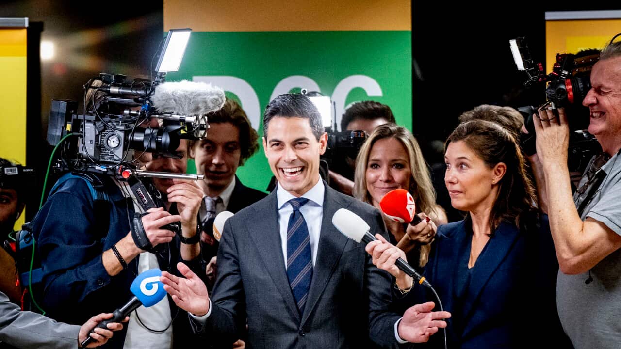 A man wearing a suit and smiling while being interviewed in front of TV cameras