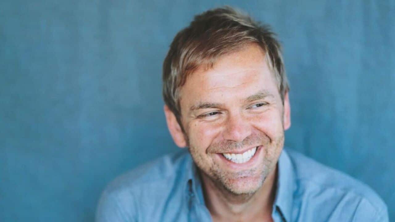 A man smiling in front of a blue background