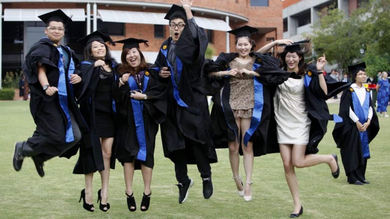 Chinese students studying abroad dressed in academic gowns pose during a graduation photo shoot at Curtin University in Bentley, Perth.