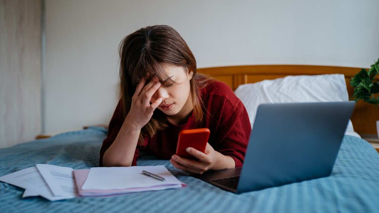 Stressed young woman using smartphone on her bed