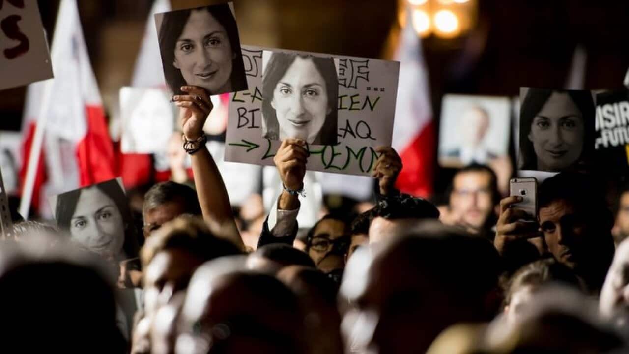 Protesters hold photos during a protest outside the office of the PM of Malta