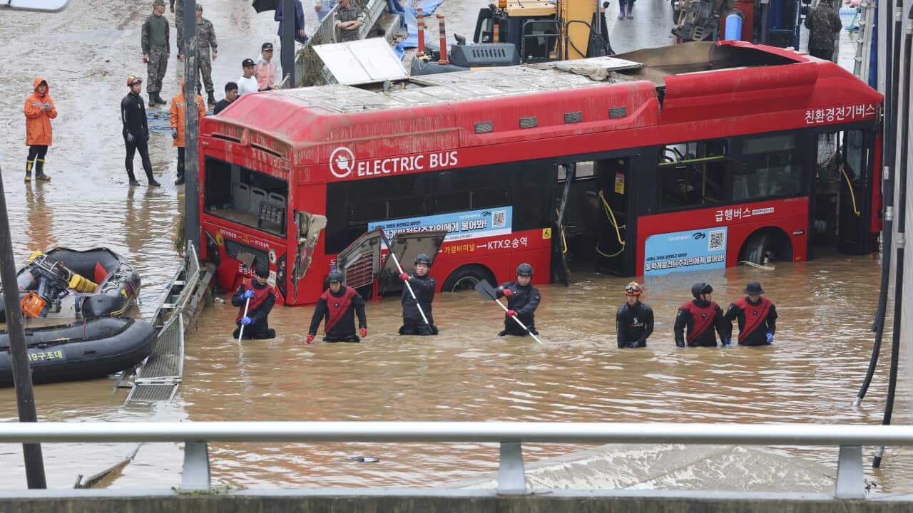 An overhead photo shows a bus partially submerged in floodwaters, while a search and rescue party wades through waist-high water