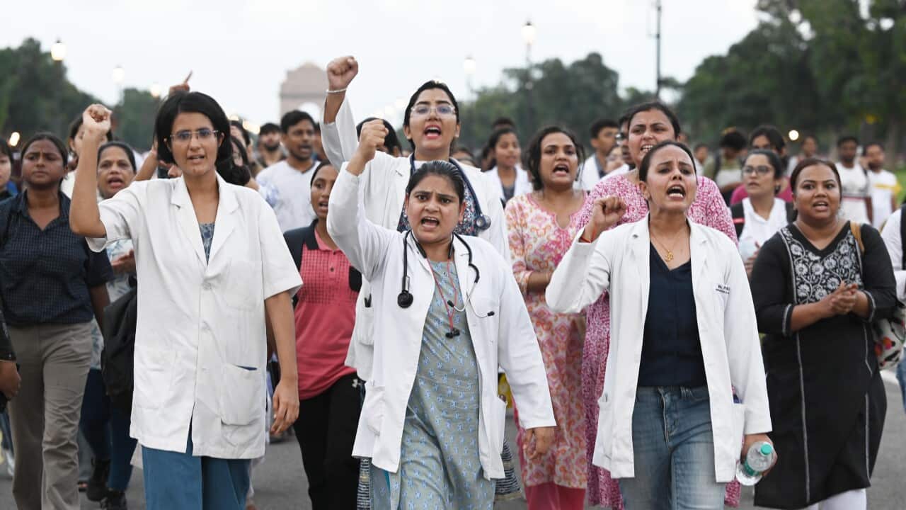 A large group of women, some wearing doctor uniforms, protesting with their fists raised in the air.