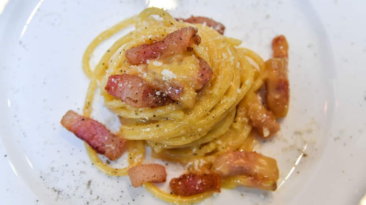 A plate of creamy carbonara pasta, with bits of sliced pork on top.