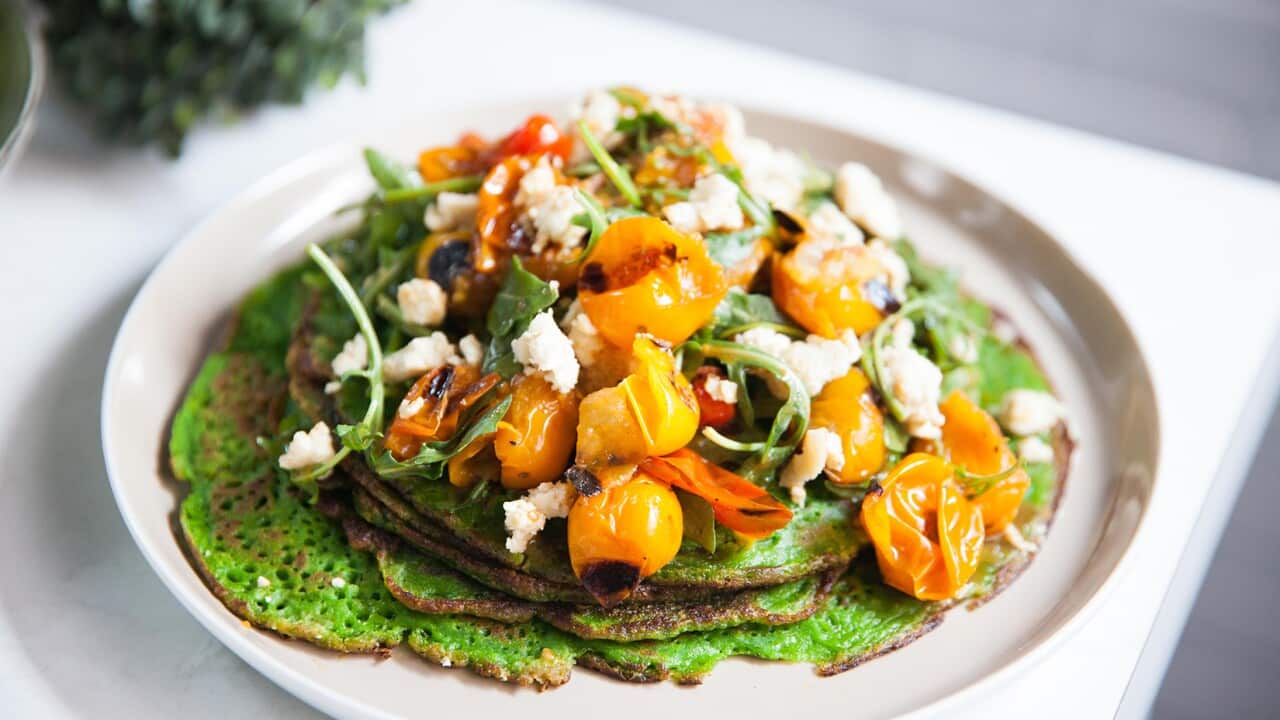 Several vibrant green thin pancakes sit on a plate, topped with a tomato, rocket and feta mixture.
