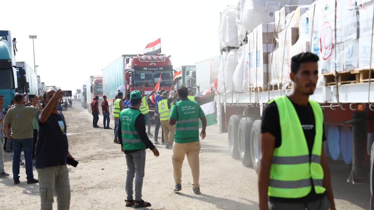 People in fluorescent vests walk alongside aid trucks lining up along dirt road