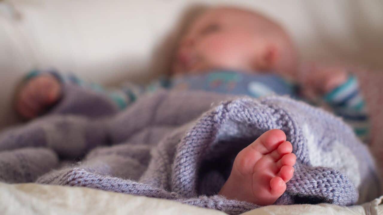 Baby lying under a blanket with toes peeking out in focus.