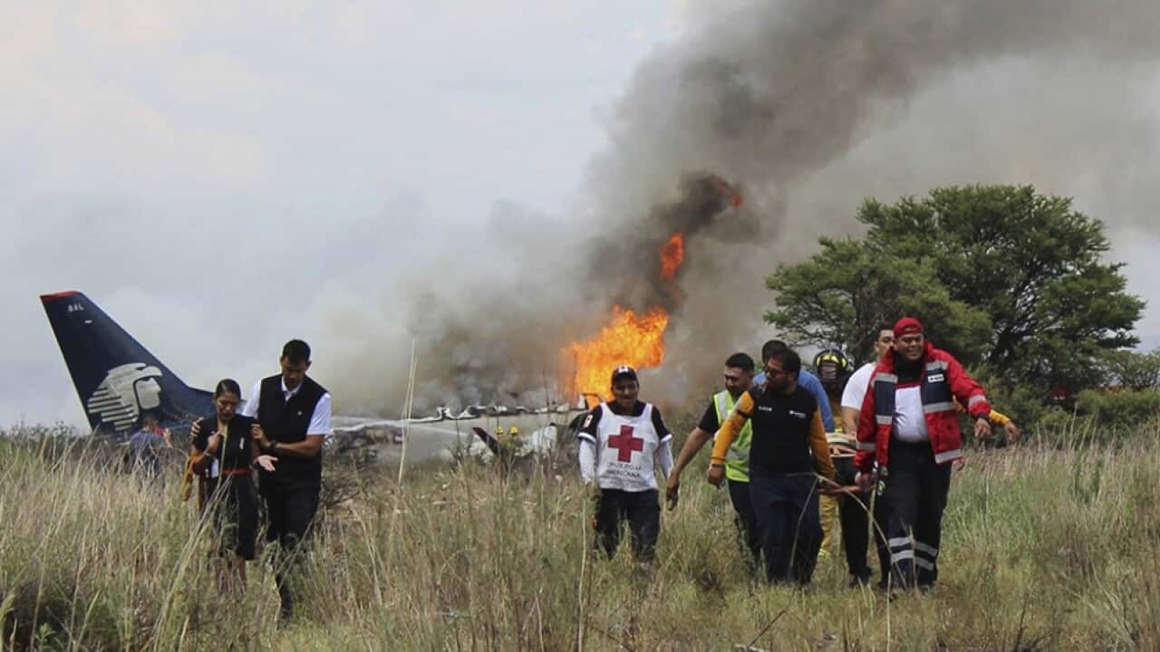 Red Cross workers and rescue workers carry an injured person on a stretcher as airline workers walk away from the site where an Aeromexico airliner crashed