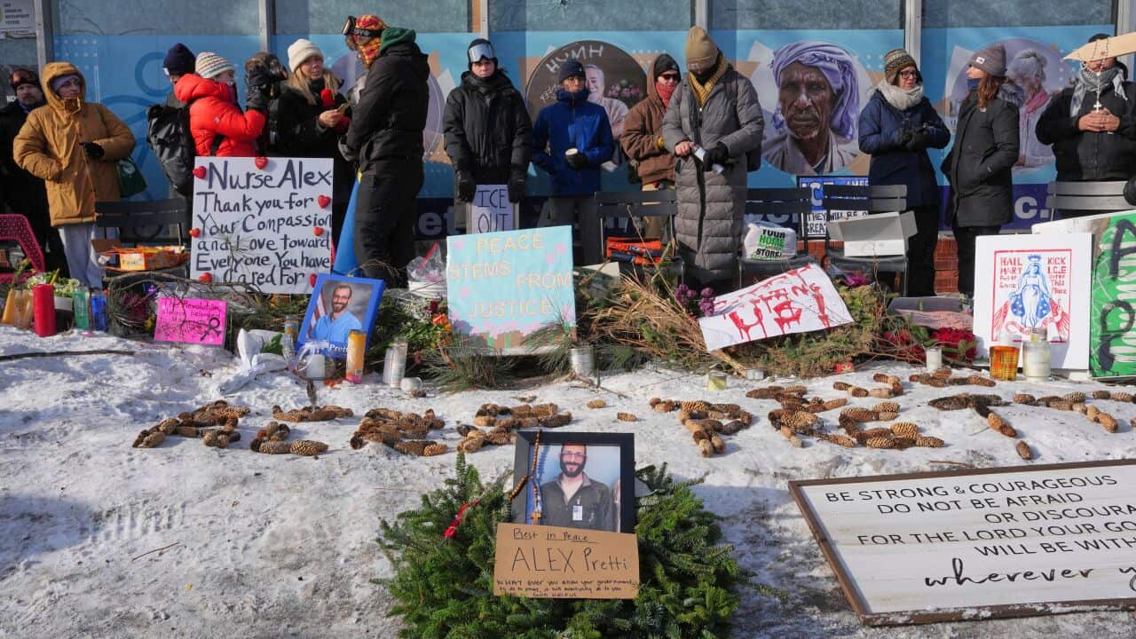 A group of people gathered around a tribute, with signs and candles.