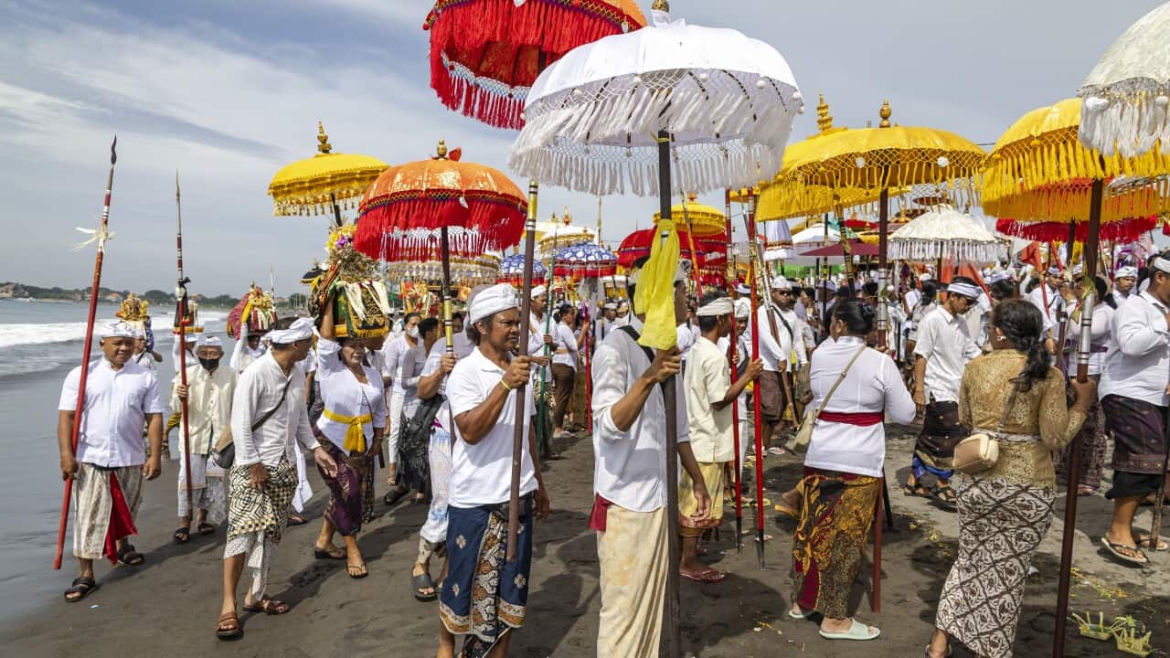 People in traditional Balinese dress holding red white and yellow umbrellas while on a beach
