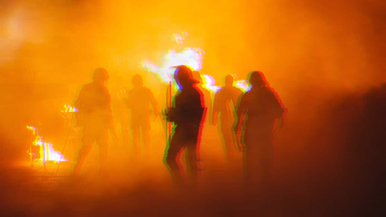 Silhouettes of armoured police officers running in front of a fire