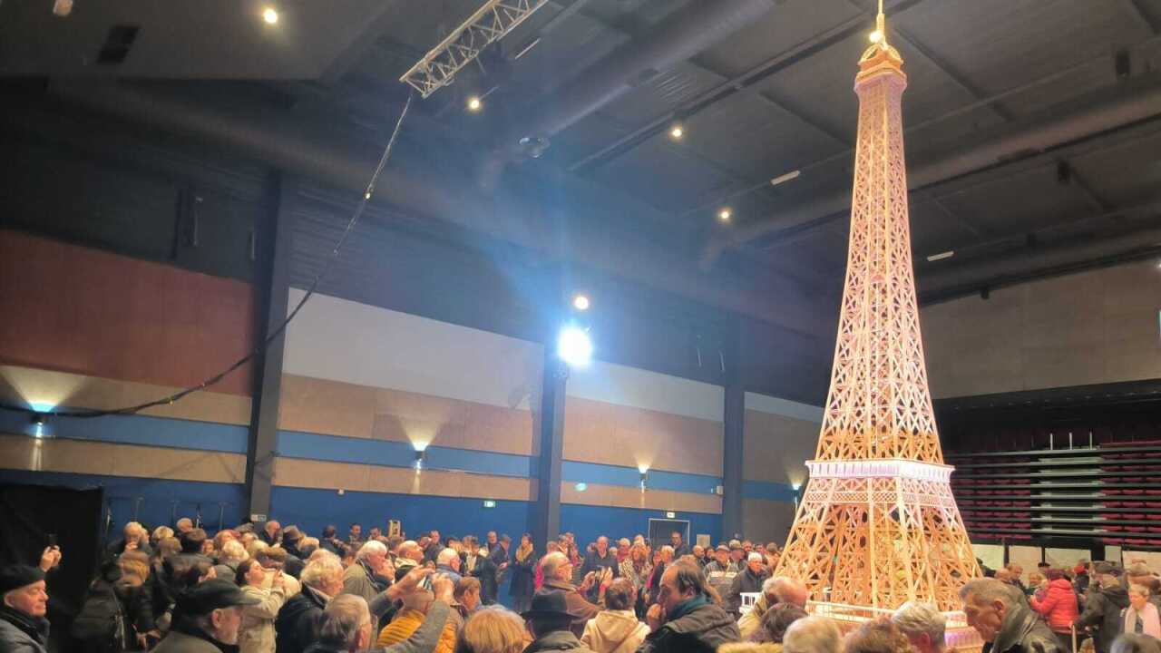 A crowd gathers around an eiffel tower made out of match sticks.