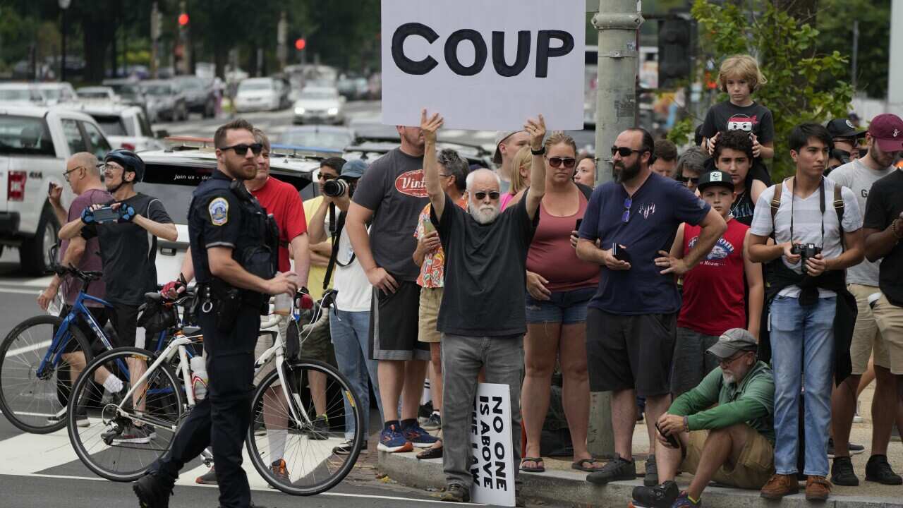 Trump supporters standing on a corner carrying a sign that says coup