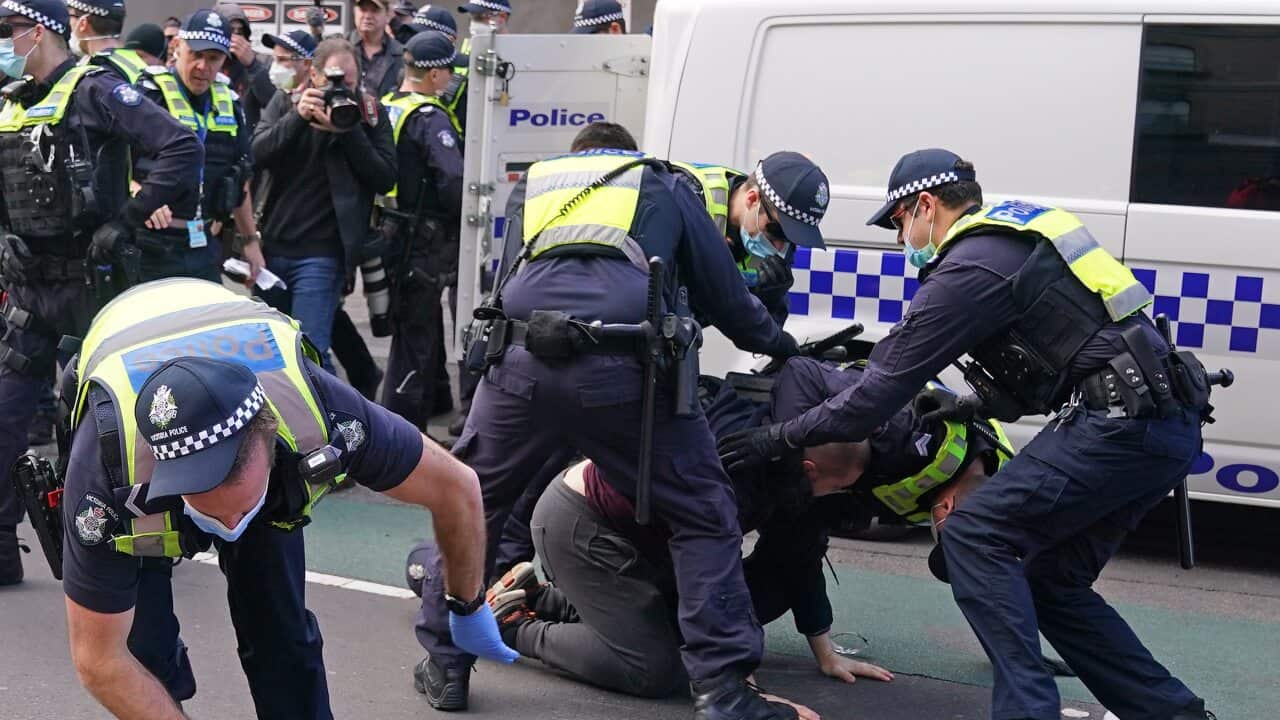 Police officers detain a man as protesters gather outside Parliament House in Melbourne.