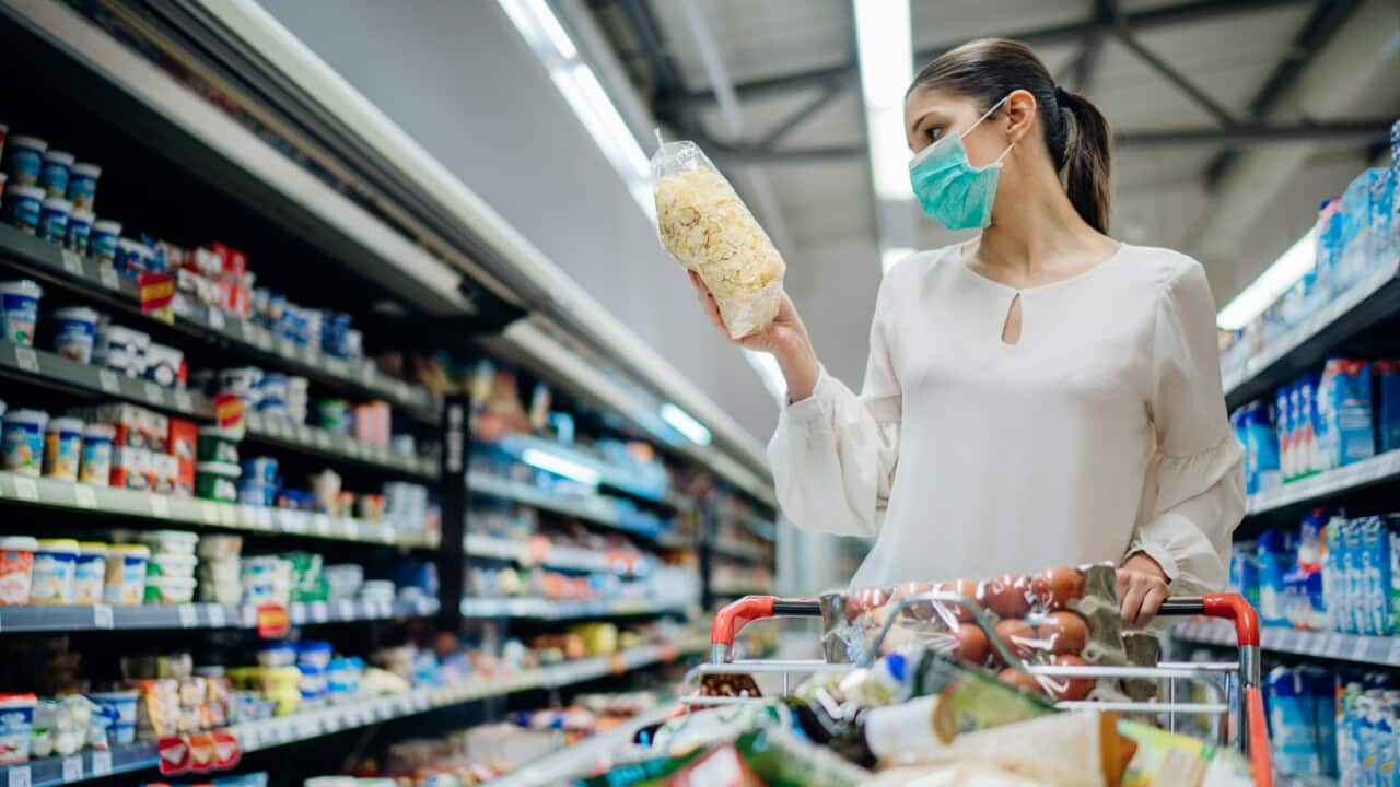 Young person with protective face mask buying groceries/supplies in the supermarket.Preparation for a pandemic quarantine due to coronavirus covid-19 outbreak.Choosing nonperishable food essentials