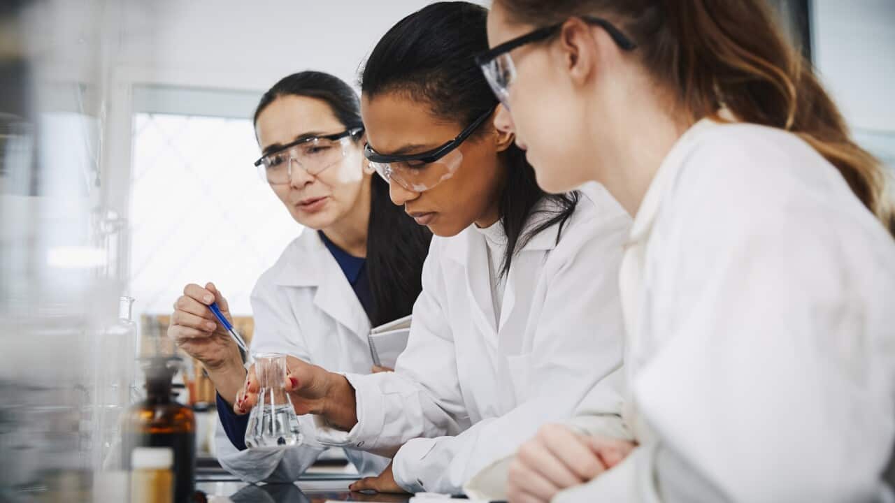 Female chemistry teacher explaining to young multi-ethnic students in laboratory