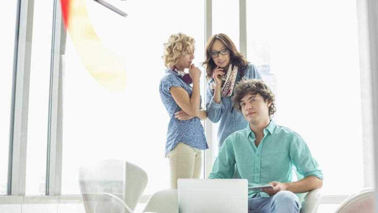  Portrait of confident businessman sitting at table with female colleagues conversing in background