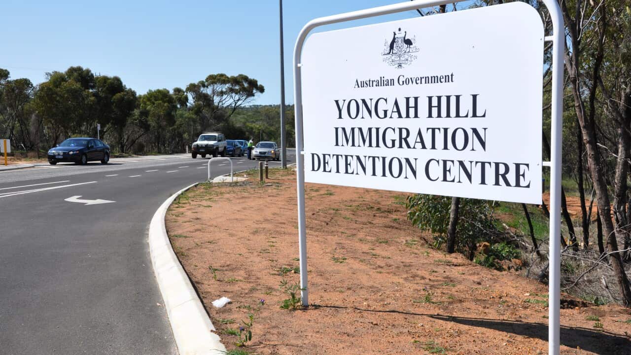 A sign that reads Yongah Hill Immigration Detention Centre on a dirt path alongside a road.