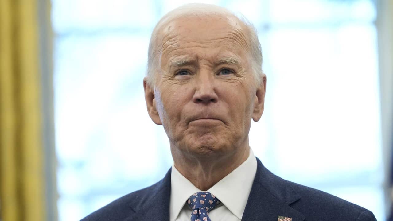 A man, wearing a blue suit and tie, looks forward with a serious expression on his face.