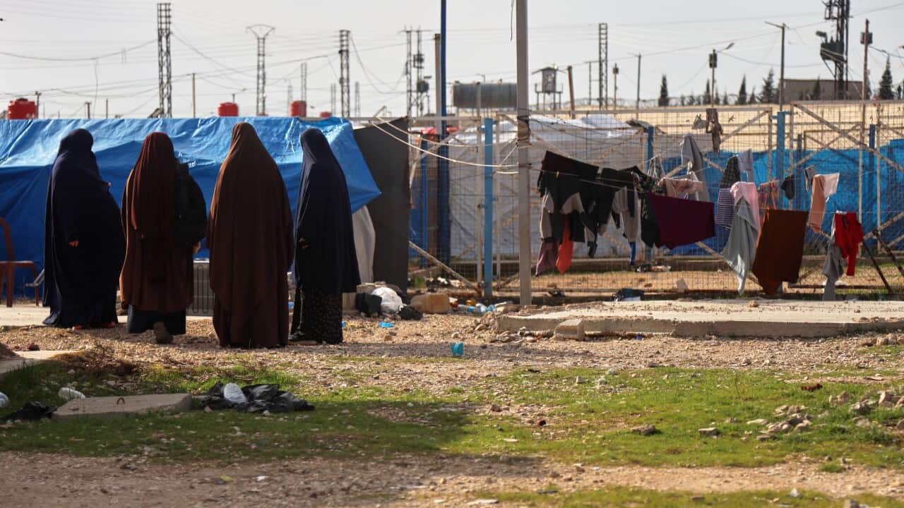Women and children walk between rows of tents in a Syrian displacement camp.