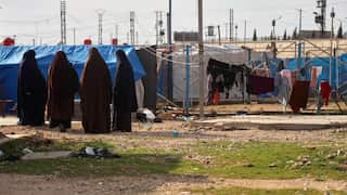 Women and children walk between rows of tents in a Syrian displacement camp.