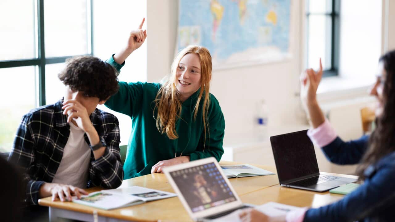 Teenage girl in school class, hand raised