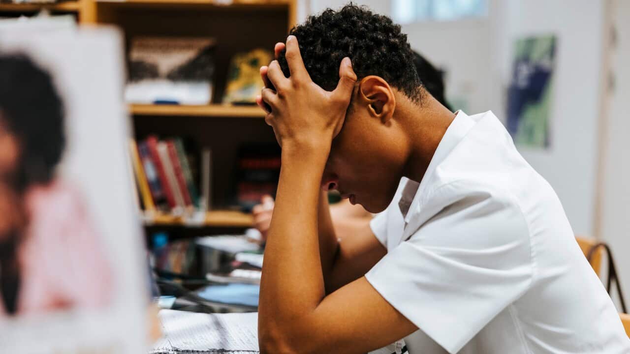 Side view of stressed teenage boy sitting with head in hand at library of school
