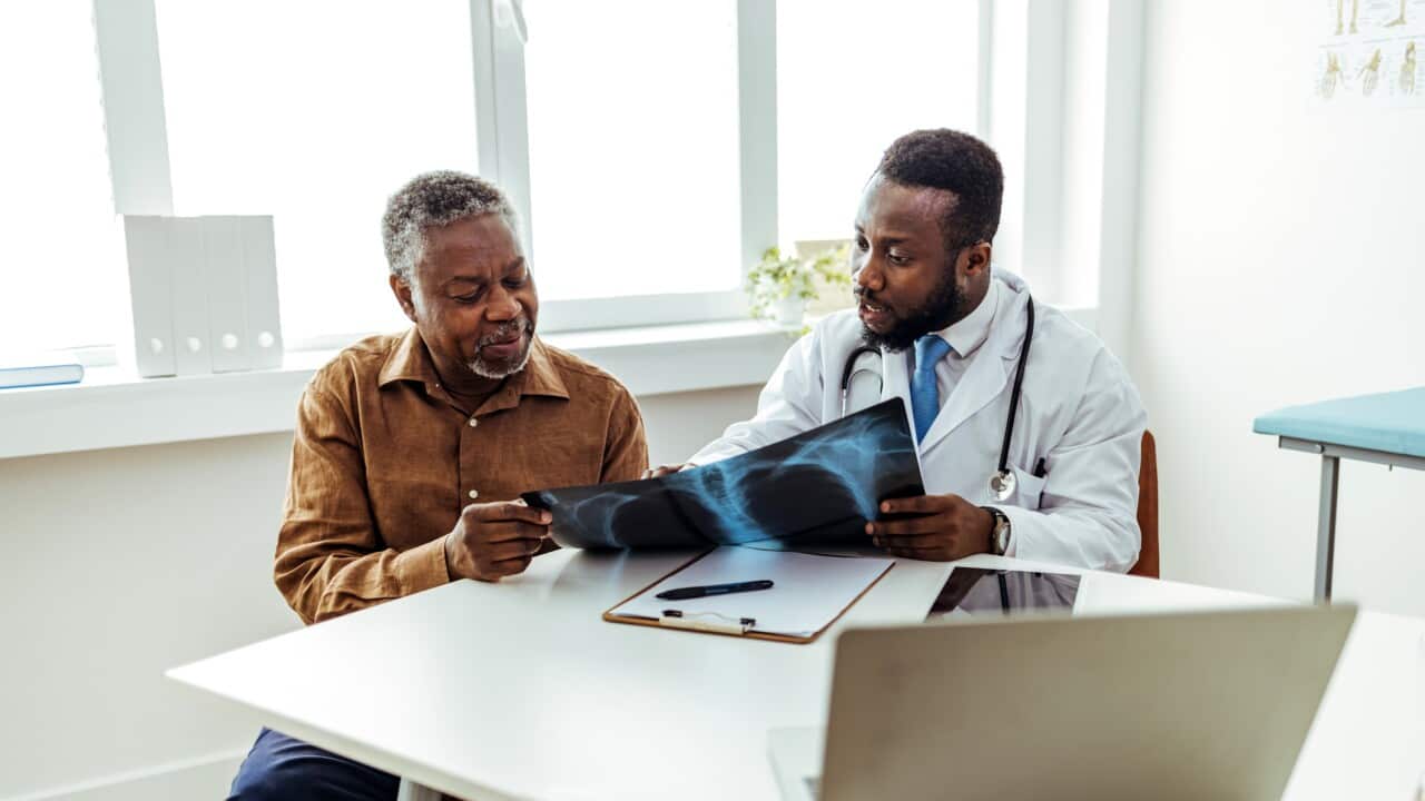 Doctor smiling and giving good news to patient, showing him lung x-ray