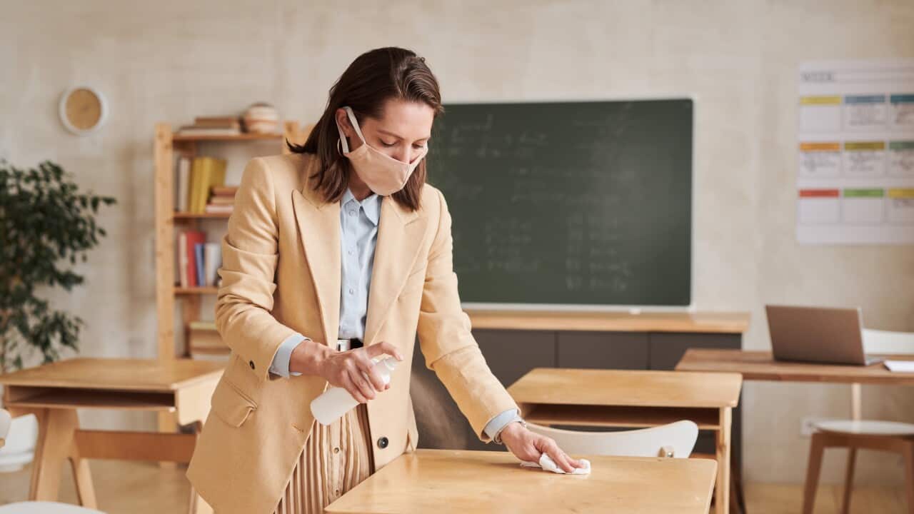A teacher who wears a mask is sanitizing table as students are ready to be back in class (Getty)