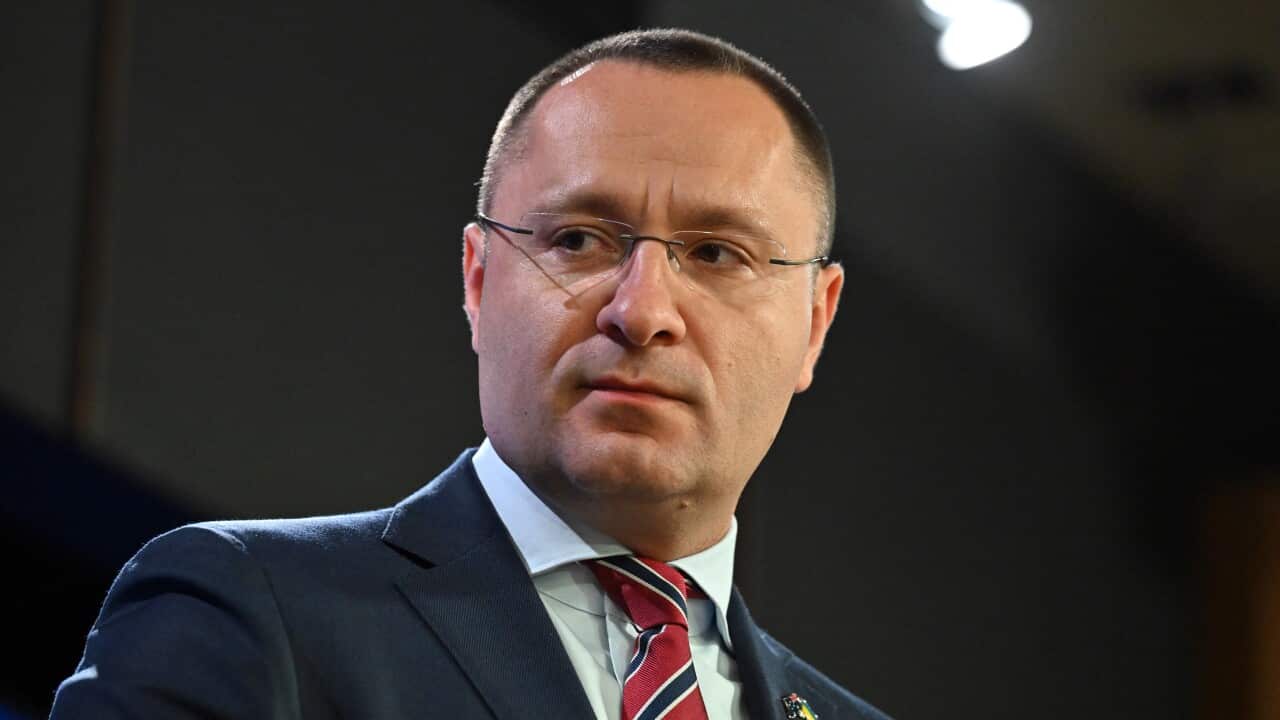 A man in glasses and a suit looks out from the camera.