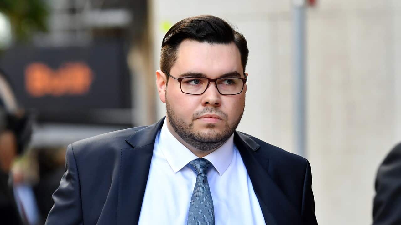 A man in a suit and glasses looks sideways as he walks.